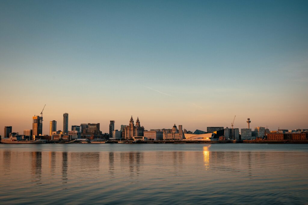 A shot of Liverpool Waterfront skyline taken from the other side of the Wirral. The sun is setting behind the buildings.